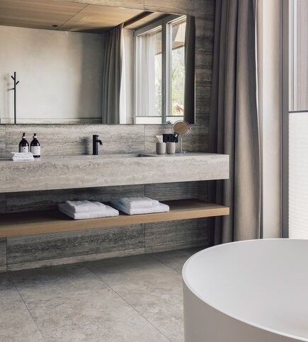 A modern bathroom with a freestanding bathtub, stone vanity, and folded towels by the window.