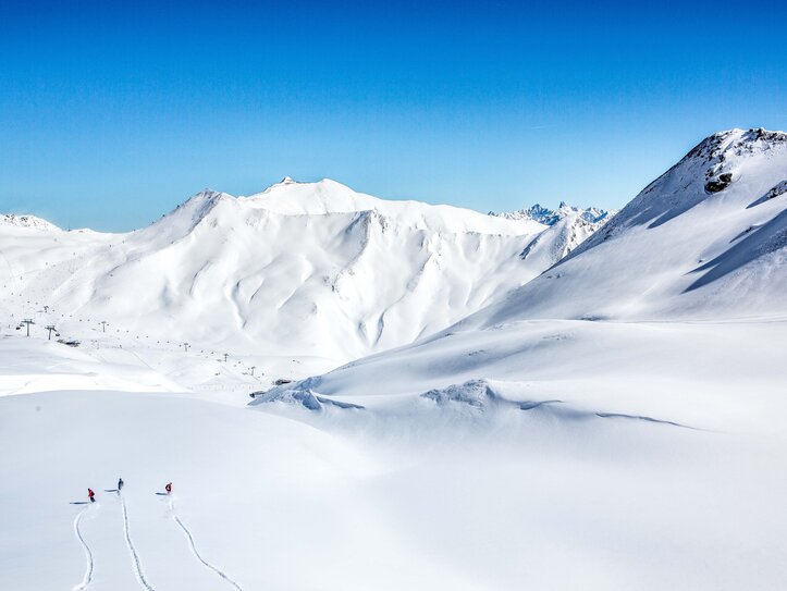 Skiurlaub in Serfaus-Fiss-Ladis Skifahrer ziehen ihre Spuren durch eine weite, verschneite Berglandschaft unter klarem Himmel.