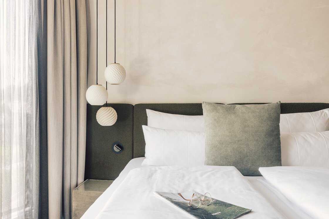 Ein stilvoll eingerichtetes Schlafzimmer mit großem Bett, Kissen und Hängeleuchten neben schweren Vorhängen.