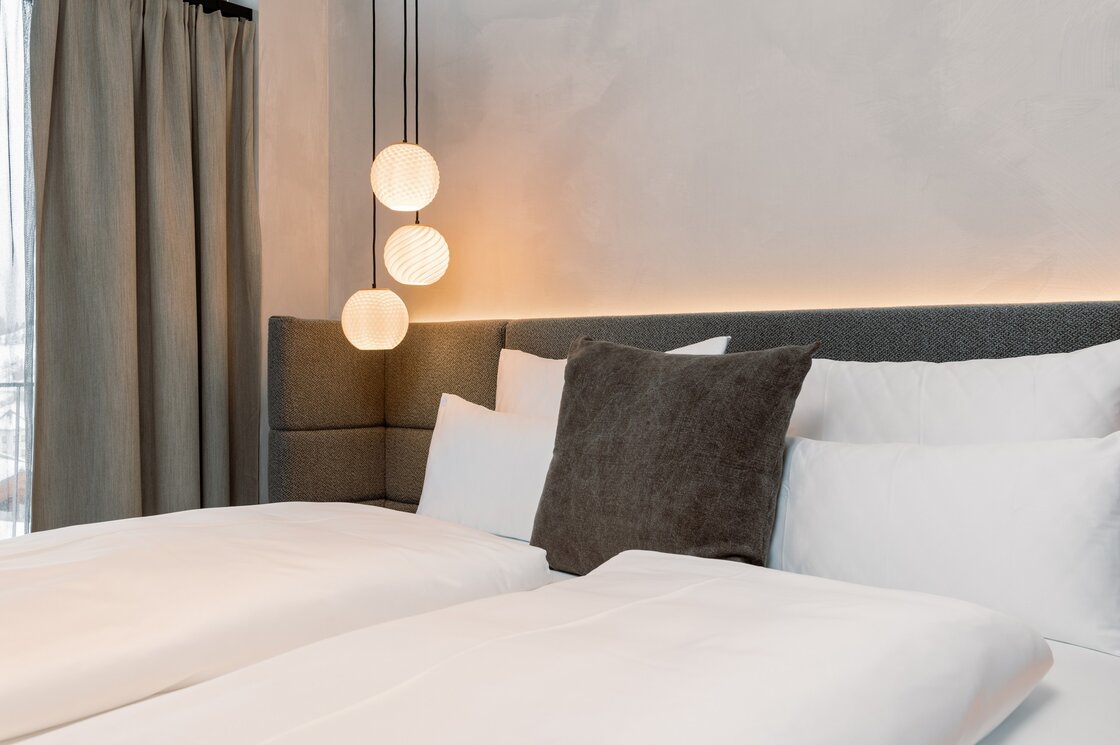 Ein modern gestaltetes Schlafzimmer mit großem Bett, Kissen und drei hängenden Leuchten neben Vorhängen.