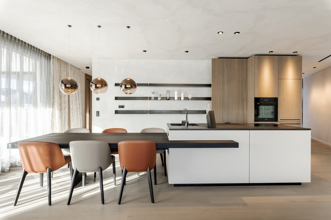 Helle Apartmentküche mit großem Esstisch, Designstühlen und Kochinsel mit Holzfronten.