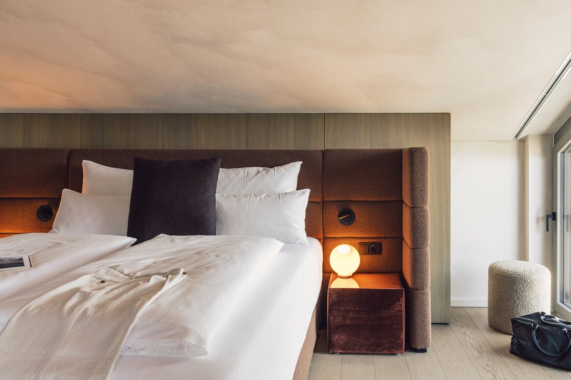 Ein modernes Schlafzimmer mit Doppelbett, gepolstertem Kopfteil und Nachttischlampe neben großen Fenstern.
