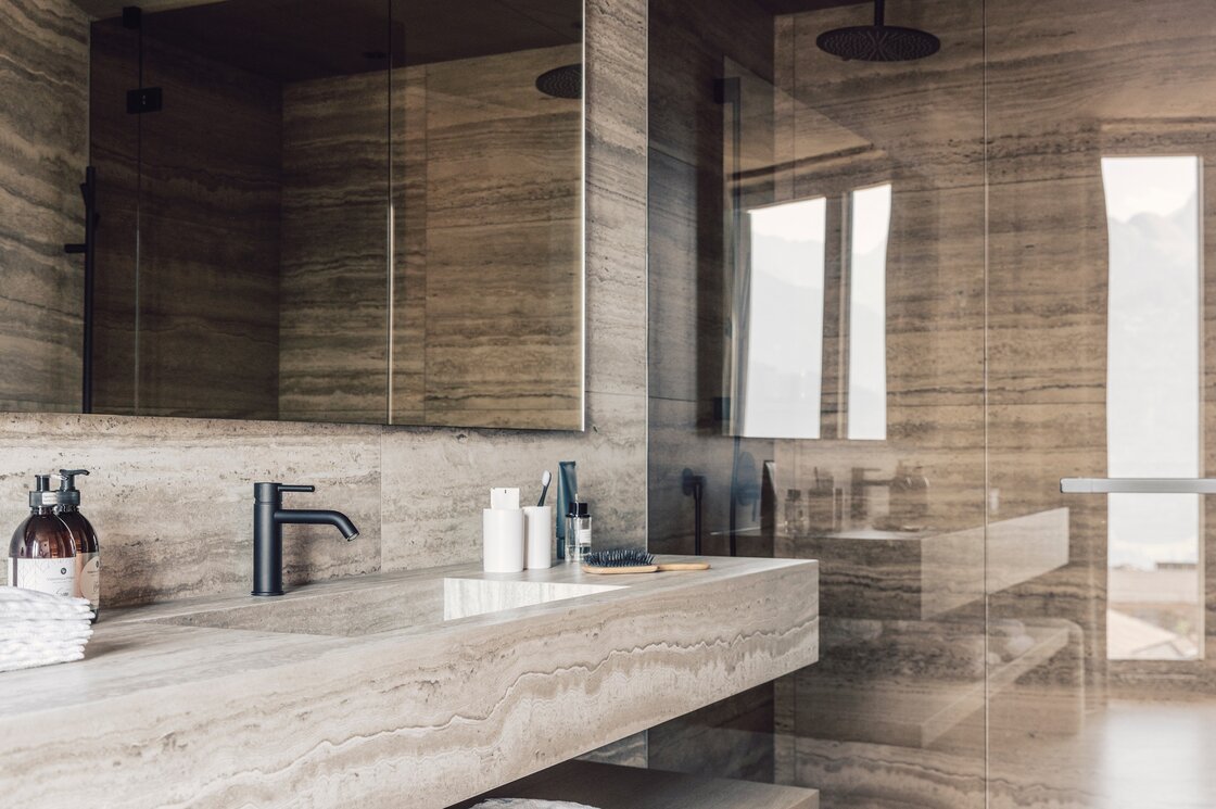 Ein modernes Badezimmer mit Walk-in-Dusche, Steinoptik-Wänden und großem Spiegel.