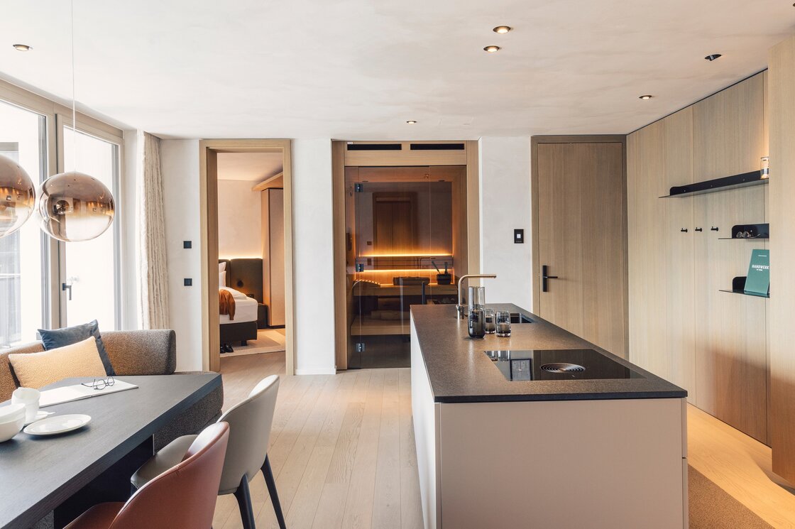 Die moderne Apartmentküche mit Wohnbereich zeigt helle Holztöne, einen Essbereich und einen Durchgang zum Schlafzimmer.