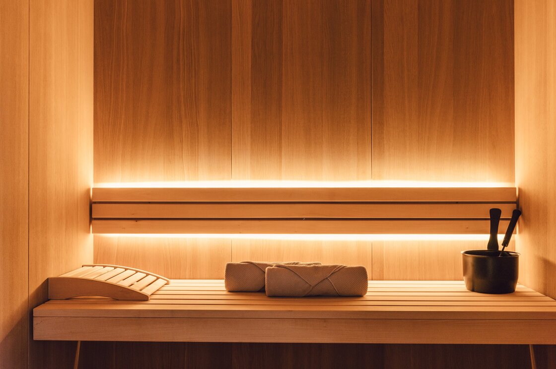 Warme Holzwand in einer privaten Sauna mit Liegebank, Handtüchern und Aufgusseimer.