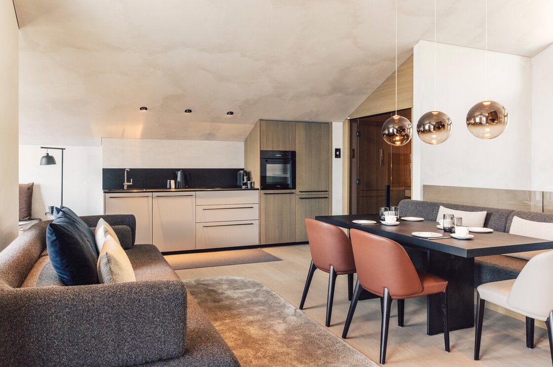 Der Wohnbereich eines modernen Penthouses mit Küchenzeile, Esstisch und Sofa unter einer schrägen Decke.
