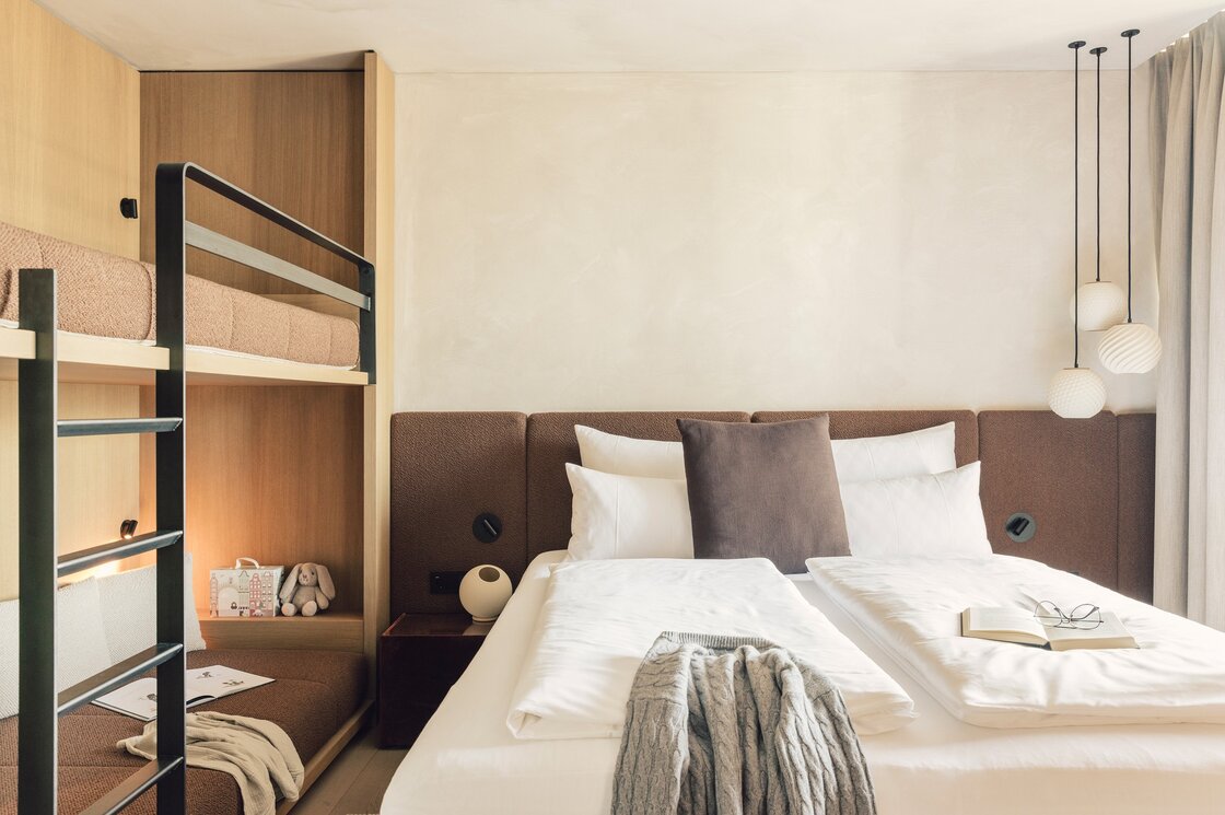 Ein stilvoll eingerichtetes Schlafzimmer mit Doppelbett, Etagenbett und warmen Holzelementen.