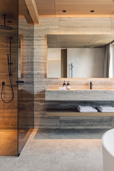 Ein modernes Badezimmer mit Dusche, Waschtisch, Spiegel und Sauna-Bereich.