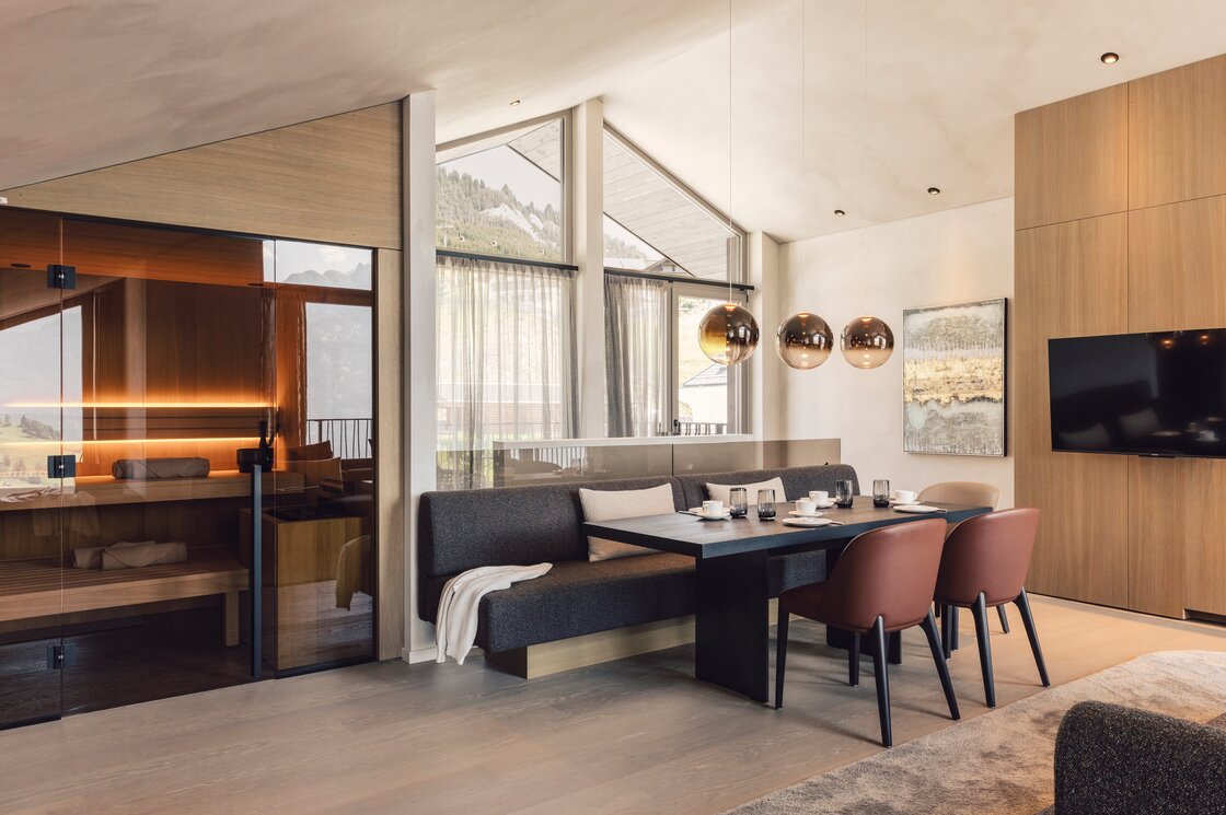 Ein moderner Essbereich mit großem Tisch, Sitzbank und Blick in die angrenzende Sauna.