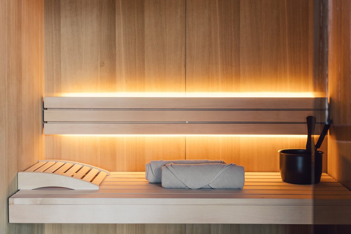 Holzsauna mit Liegefläche, Handtüchern und Aufgusseimer in warmem Licht.