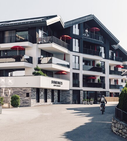Ein modernes Apartmenthaus mit Balkonen und roten Sonnenschirmen an einer ruhigen Straße in Fiss.