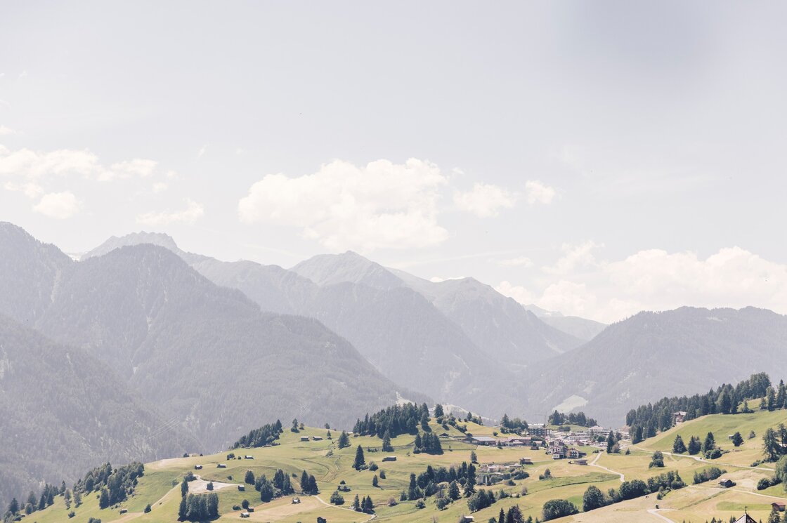 Weite Berglandschaft mit grünen Hügeln, verstreuten Bäumen und dem Ort Fiss im Tal.