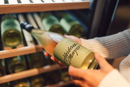 Eine Person hält eine Flasche Wein vor einem geöffneten Weinkühlschrank.