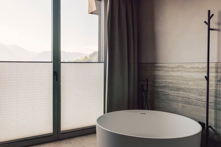 Ein modernes Bad mit freistehender Wanne und Blick auf die Berge durch große Fenster.