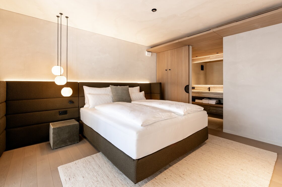 Ein modern eingerichtetes Schlafzimmer mit Doppelbett, warmen Pendelleuchten und Blick ins angrenzende Bad.