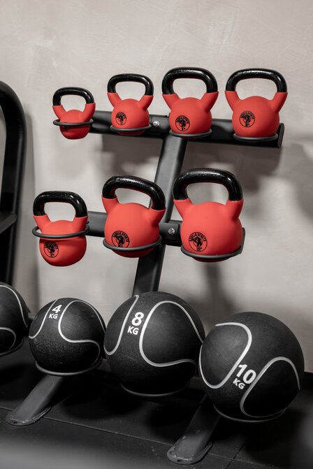 Mehrere rote Kettlebells und schwarze Medizinbälle stehen ordentlich auf einem Regal im Fitnessraum.