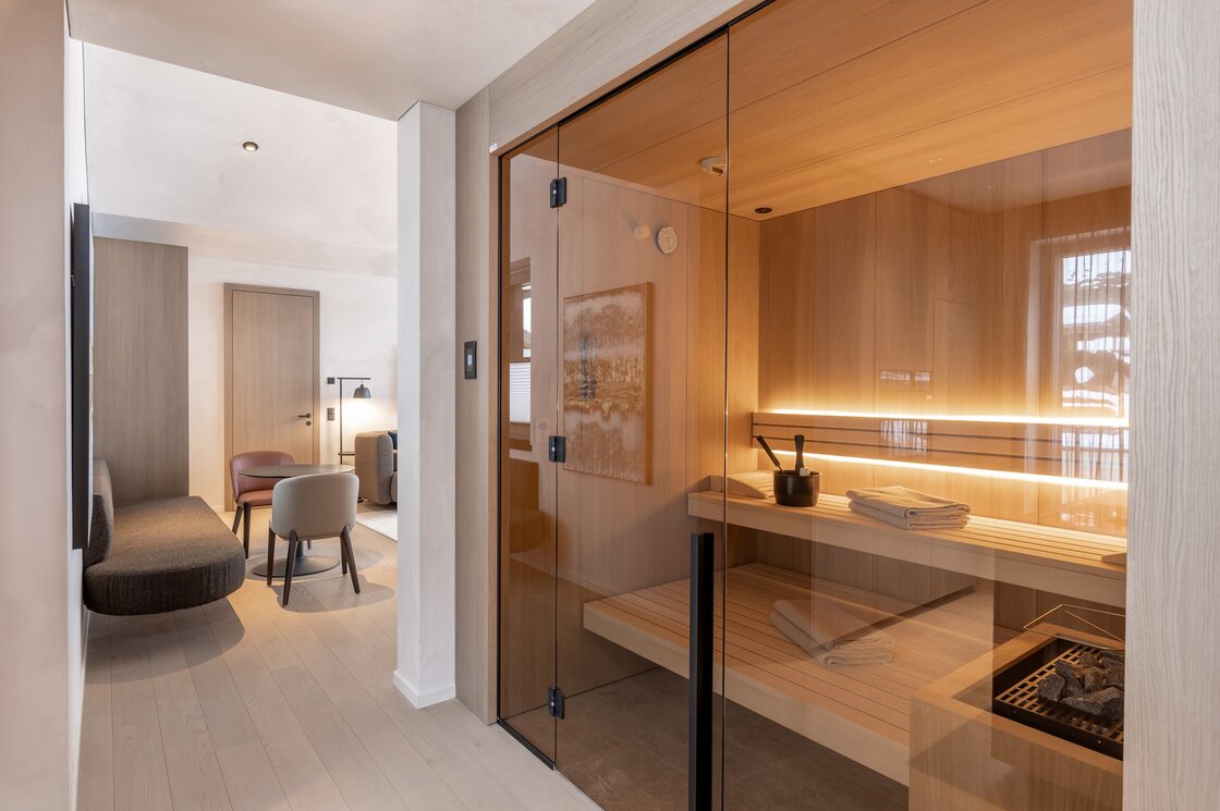 Ein moderner Wohnbereich mit Glasfront zur privaten Sauna und Sitzmöbeln im Penthouse.