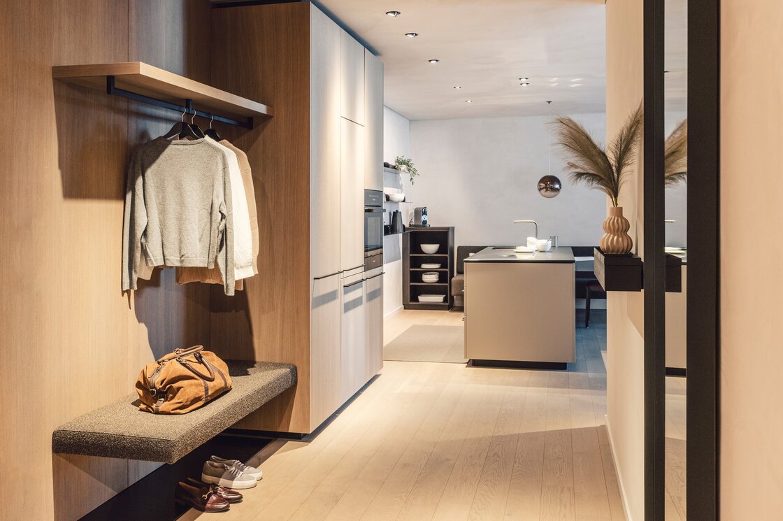 Ein moderner Eingangsbereich mit Garderobe, Bank, Küchenzeile und warmen Holzelementen.