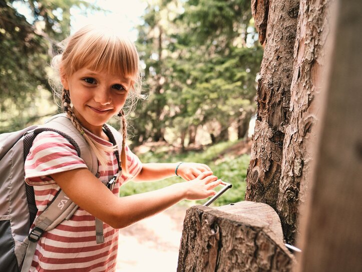 Mädchen beim Wandern im Wald in Fiss Ein Mädchen mit Rucksack steht im Wald und spielt an einer Holzkonstruktion beim Wandern.