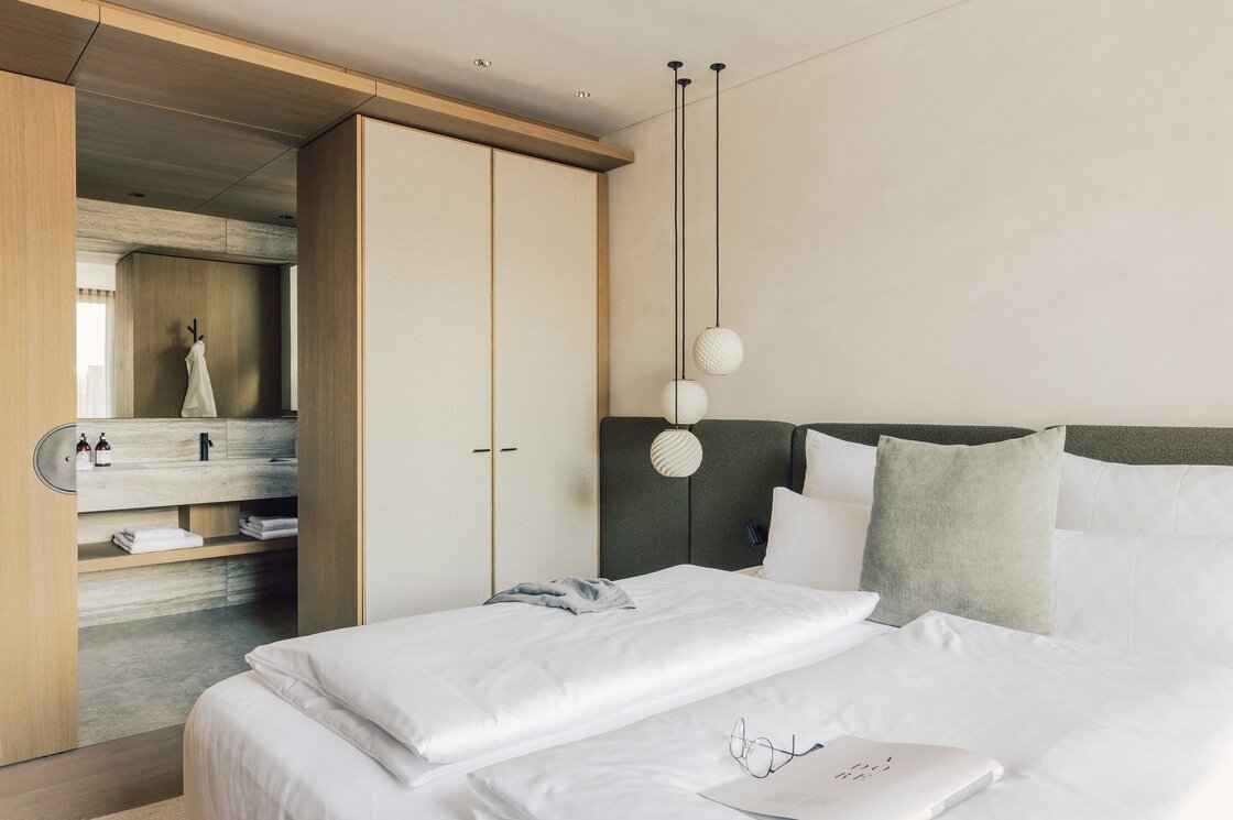 Ein modernes Schlafzimmer im Apartment mit Doppelbett, Hängeleuchten und offenem Badbereich.
