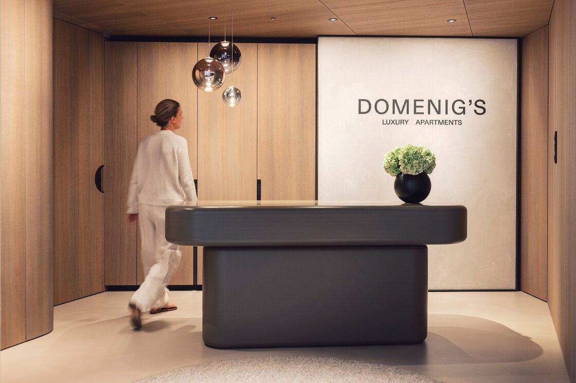 Eine Person geht durch den Empfangsbereich mit Holzverkleidung und moderner Theke bei Domenig's Luxury Apartments.