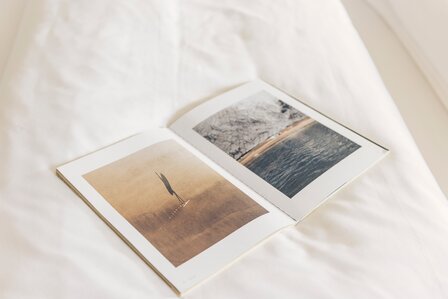 Ein offenes Fotobuch liegt auf einem hellen Bett mit weißen Kissen und zeigt zwei großformatige Bilder.