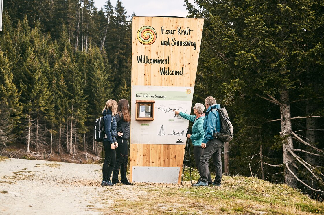 Wanderer lesen die Infotafel am Fisser Kraft- und Sinnesweg im Wald.