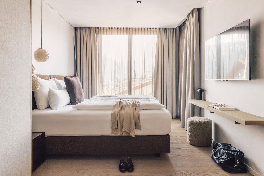 Ein helles Schlafzimmer mit Doppelbett, großen Vorhängen und Schreibtisch in einem Apartment in Fiss.