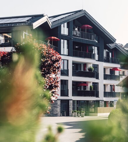 Außenansicht der Luxury Apartments mit Balkonen, roten Sonnenschirmen und dunkler Holzfassade in Fiss.