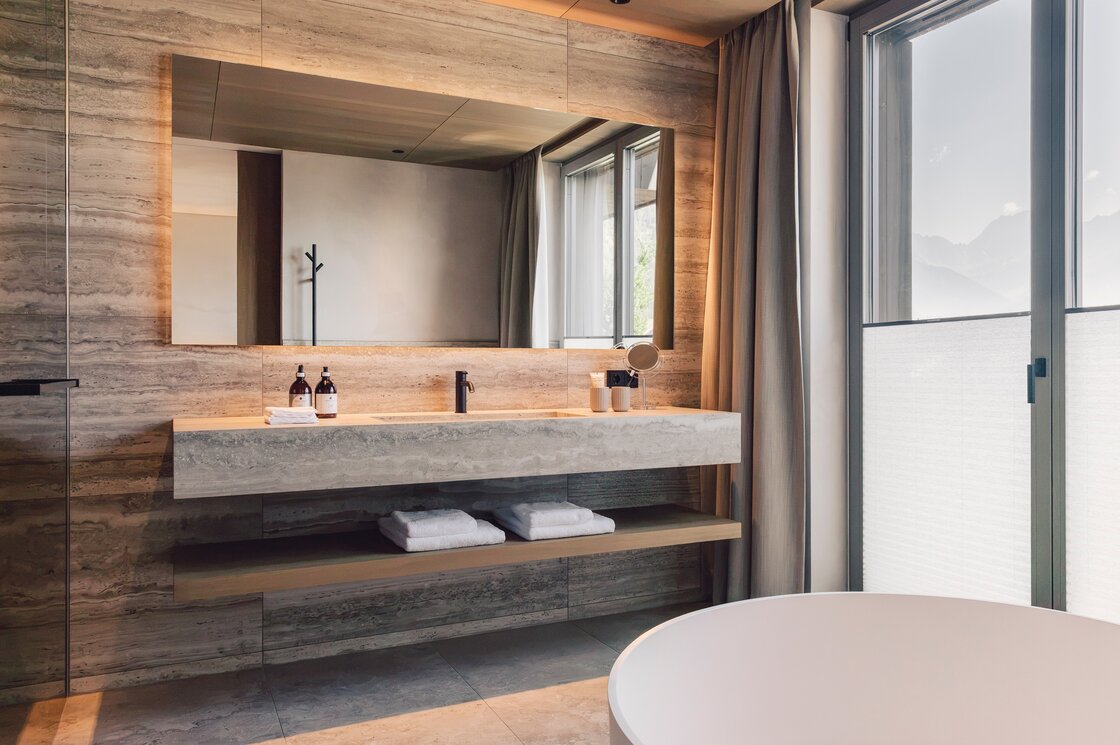 Ein modernes Badezimmer mit Waschtisch, großer Spiegelwand und freistehender Badewanne am Fenster.