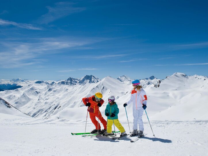 Skifahren mit Kindern in Serfaus-Fiss-Ladis Drei Skifahrer stehen mit Skiern auf einem verschneiten Gipfel vor den Bergen.