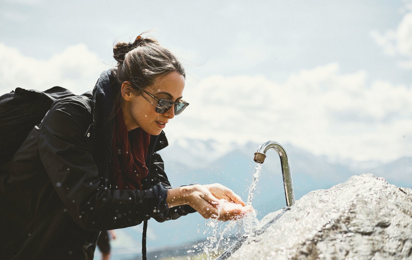 Eine Frau wäscht sich an einem Bergbrunnen die Hände im Freien.