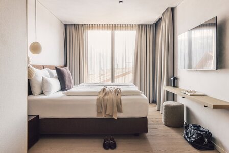 Ein helles Schlafzimmer mit Doppelbett, Vorhängen und Wandfernseher in einem modernen Apartment.