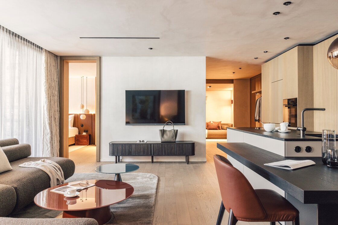 Ein moderner Wohnbereich mit offener Küche, Sofa, Fernseher und Blick ins Schlafzimmer.