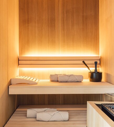 Eine helle Sauna mit Holzwänden, Liegen und Saunazubehör im Apartment.