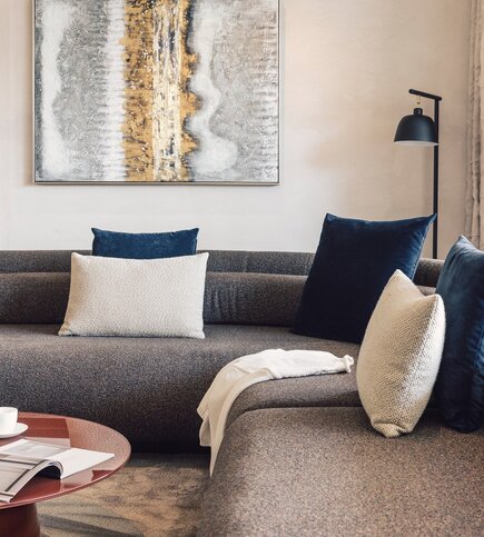 Ein gemütliches Wohnzimmer mit Sofa, Kissen, Stehlampe und abstraktem Wandbild.