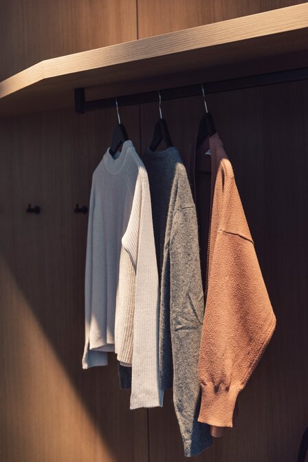 Mehrere Pullover hängen in einem offenen Kleiderschrank mit Holzoberfläche.