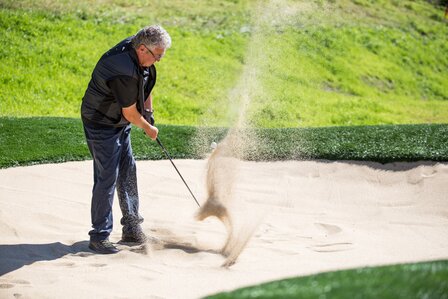 Ein Mann schlägt einen Golfball aus dem Bunker auf einem gepflegten Golfplatz.