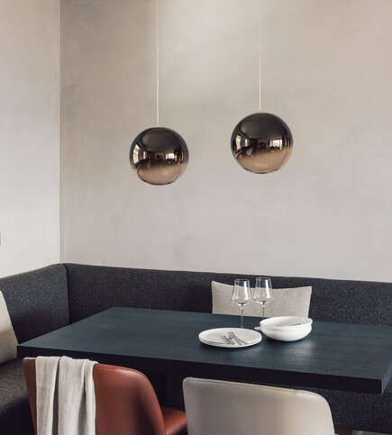 Ein moderner Essbereich im Apartment mit dunkler Bank, Tisch und zwei Pendelleuchten.