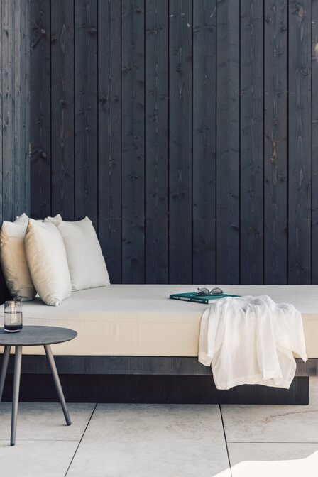 Ein helles Daybed mit Kissen, Tisch und Buch vor dunkler Holzverkleidung im Apartment.