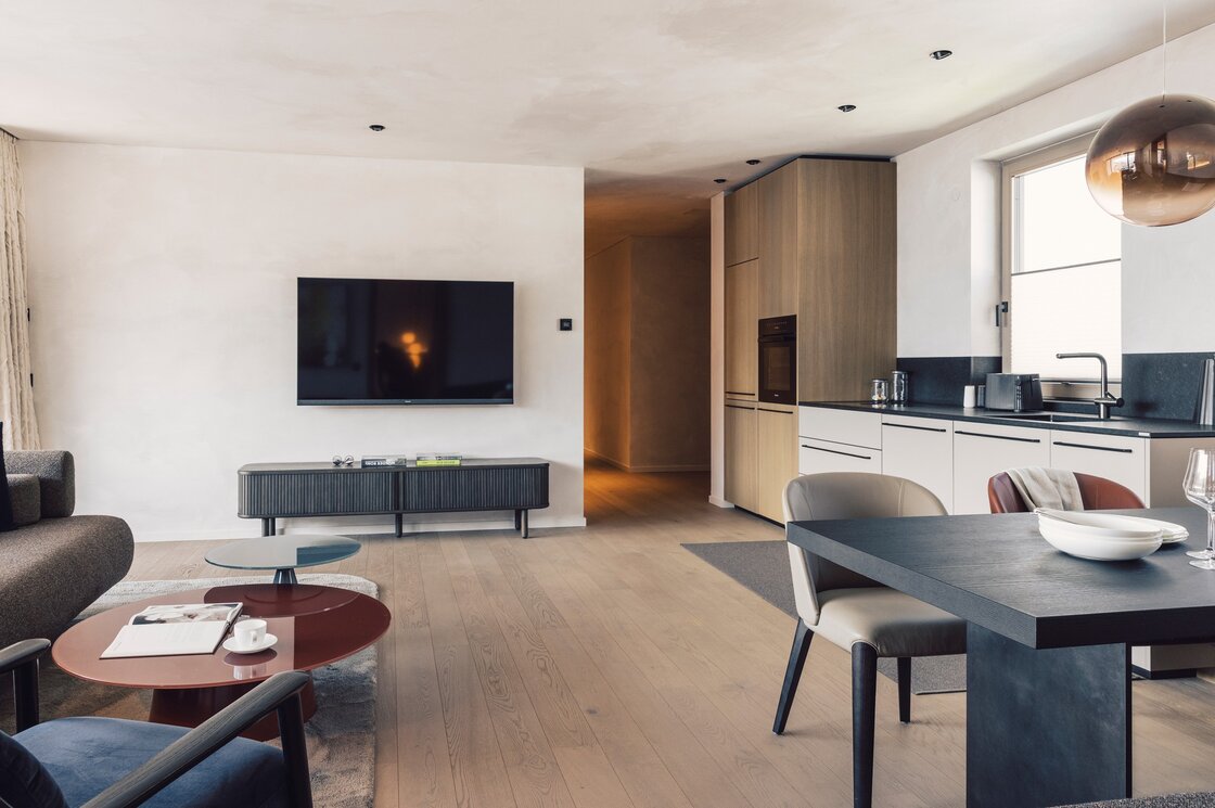 Wohnbereich und Küchenzeile in einem modernen Apartment mit Esstisch, Sofa und TV.