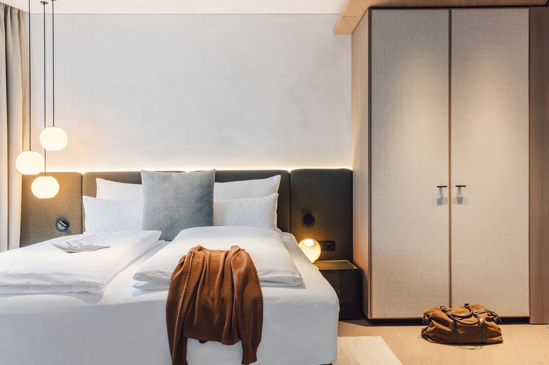 Ein stilvoll eingerichtetes Schlafzimmer mit Doppelbett, Schrank und warmen Pendelleuchten.