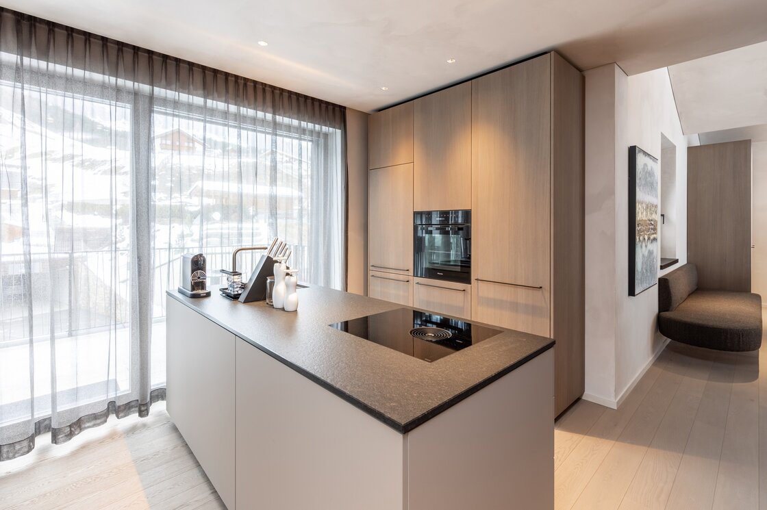 Moderne Penthouse-Küche mit Kochinsel, großen Fenstern und Blick auf die verschneiten Berge in Fiss.