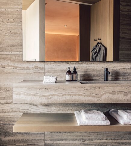 Ein modernes Badezimmer mit Natursteinwand, Waschtisch, Handtüchern und Spiegel.