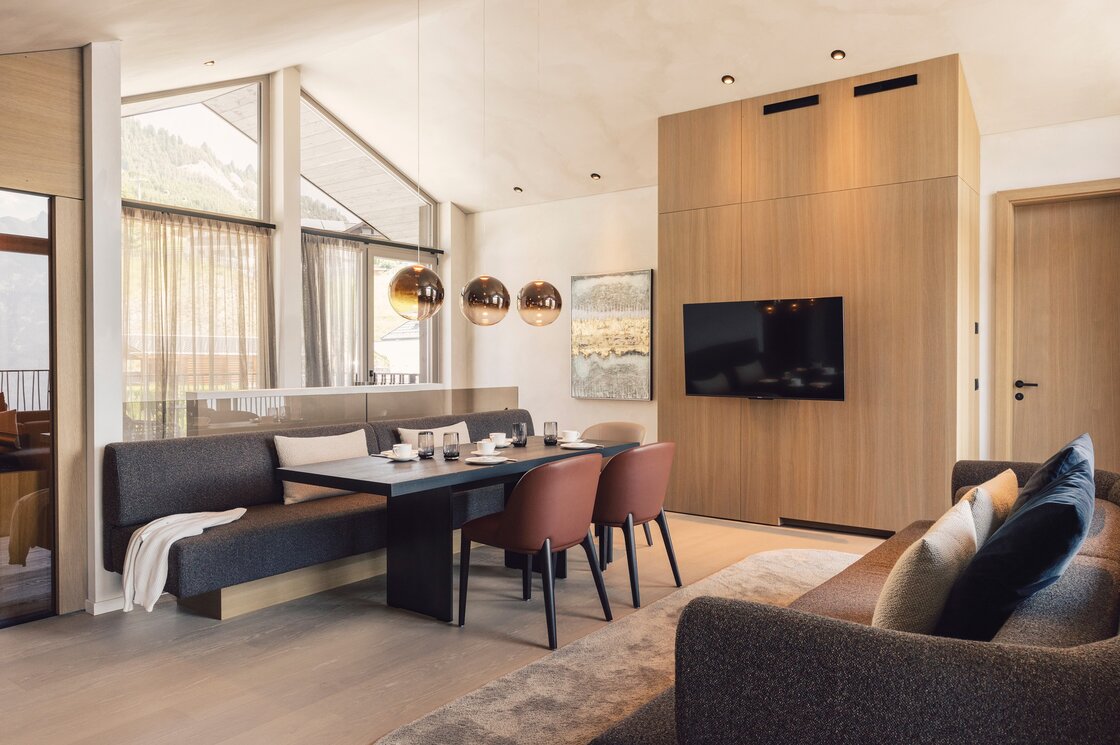 Gemütlicher Wohn- und Essbereich eines Penthouse mit großen Fenstern und Blick auf die Berge.