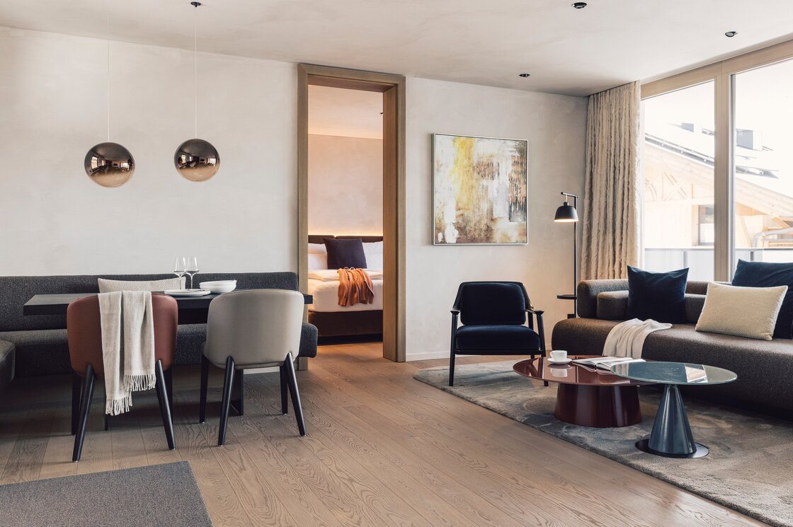 Der offene Wohnbereich eines stilvollen Apartments mit Essplatz, Sofa, Sessel und Blick ins Schlafzimmer.