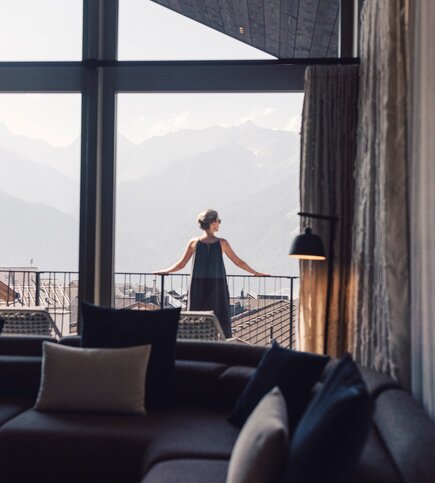 Eine Frau steht auf dem Balkon eines Apartments und blickt in die Berglandschaft.