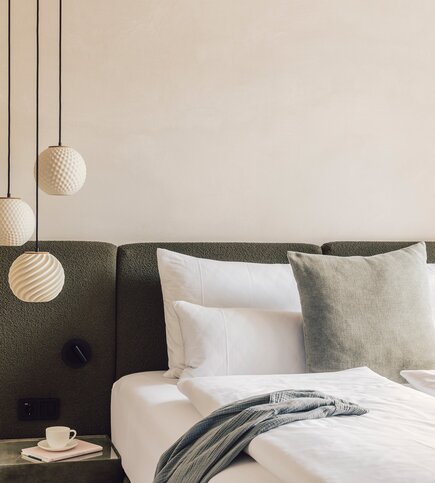 Ein stilvoll eingerichtetes Schlafzimmer mit Doppelbett, gepolstertem Kopfteil und hängenden Leuchten.