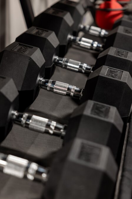 Mehrere schwarze Kurzhanteln liegen ordentlich auf einem Rack im Fitnessstudio.