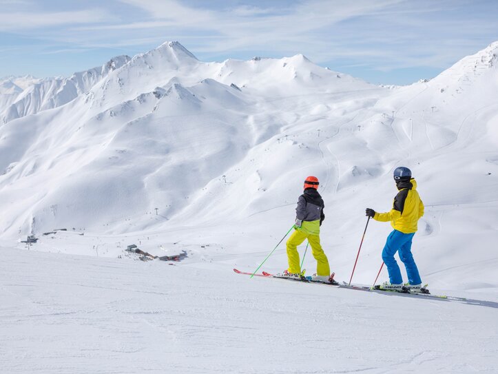 Skifahrer mit Bergblick in Serfaus-Fiss-Ladis Zwei Skifahrer stehen auf einer verschneiten Piste mit weitem Blick auf die Berge.